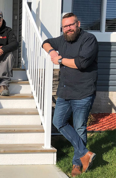 Person smiling and leaning on rail on steps of house.