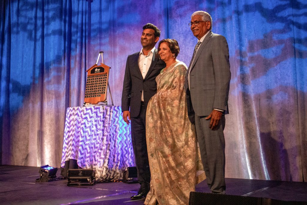 Photo of Radhe, Krishna and the presenter on stage for Hall of Fame.