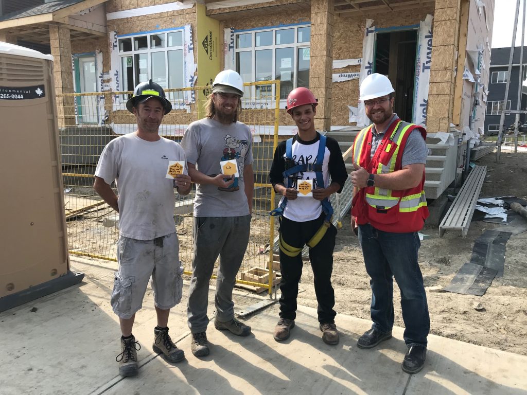 4 smiling construction workers holding yellow hexagon sheets.